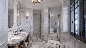 Un baño lujoso con pisos y paredes de mármol, un lavamanos doble, una ducha a pie y un espejo grande.