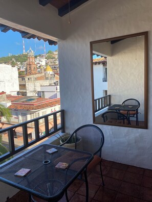Ein Balkon mit Tisch und Stühlen, einem Blumentopf und Blick auf eine Stadtlandschaft mit Gebäuden und einem Kirchturm.