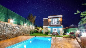 Una piscina con cubierta de madera, un muro de piedra y una casa con balcón.