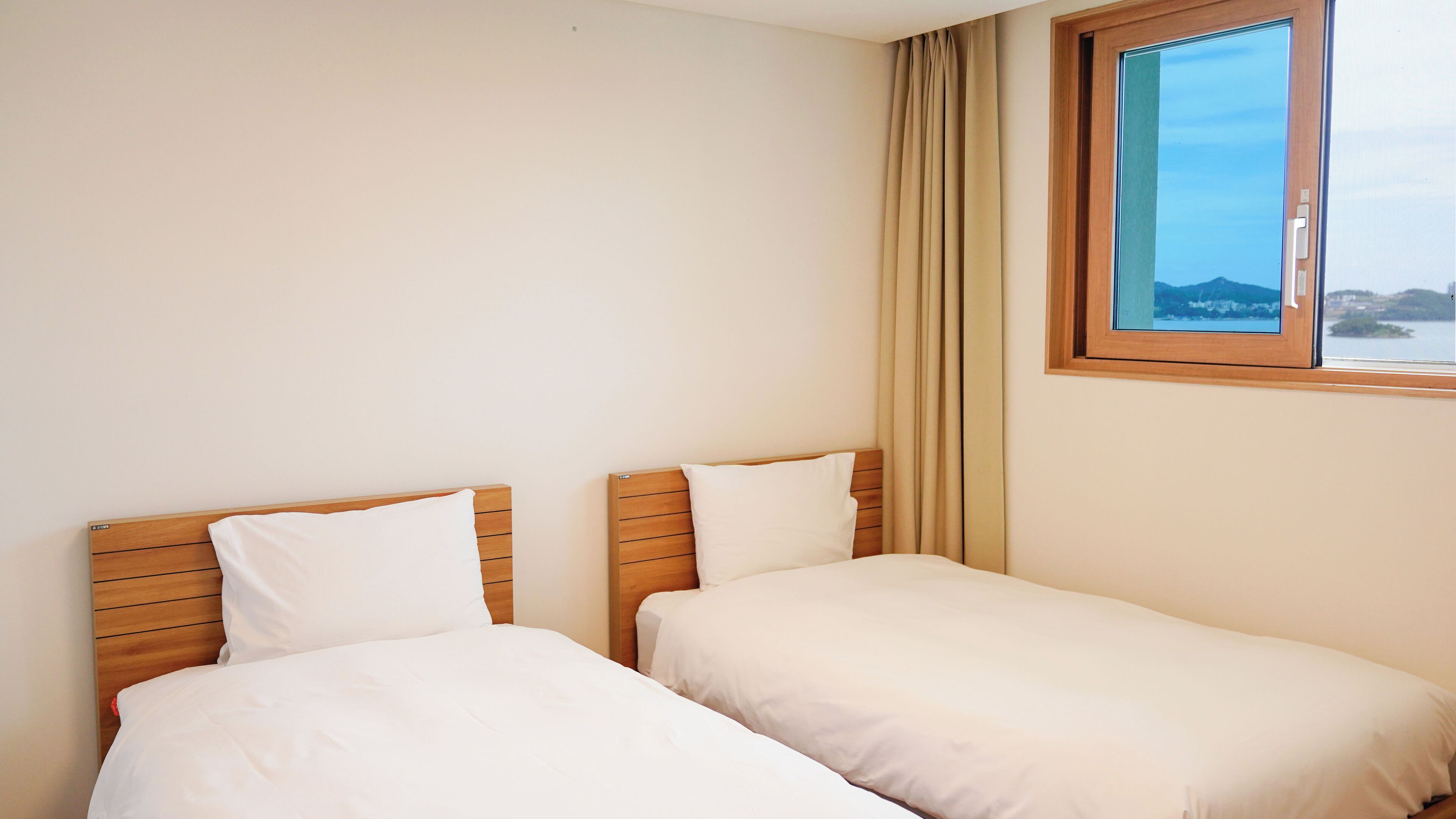 A hotel room with two single beds, a window with a view of the sea, and a curtain.