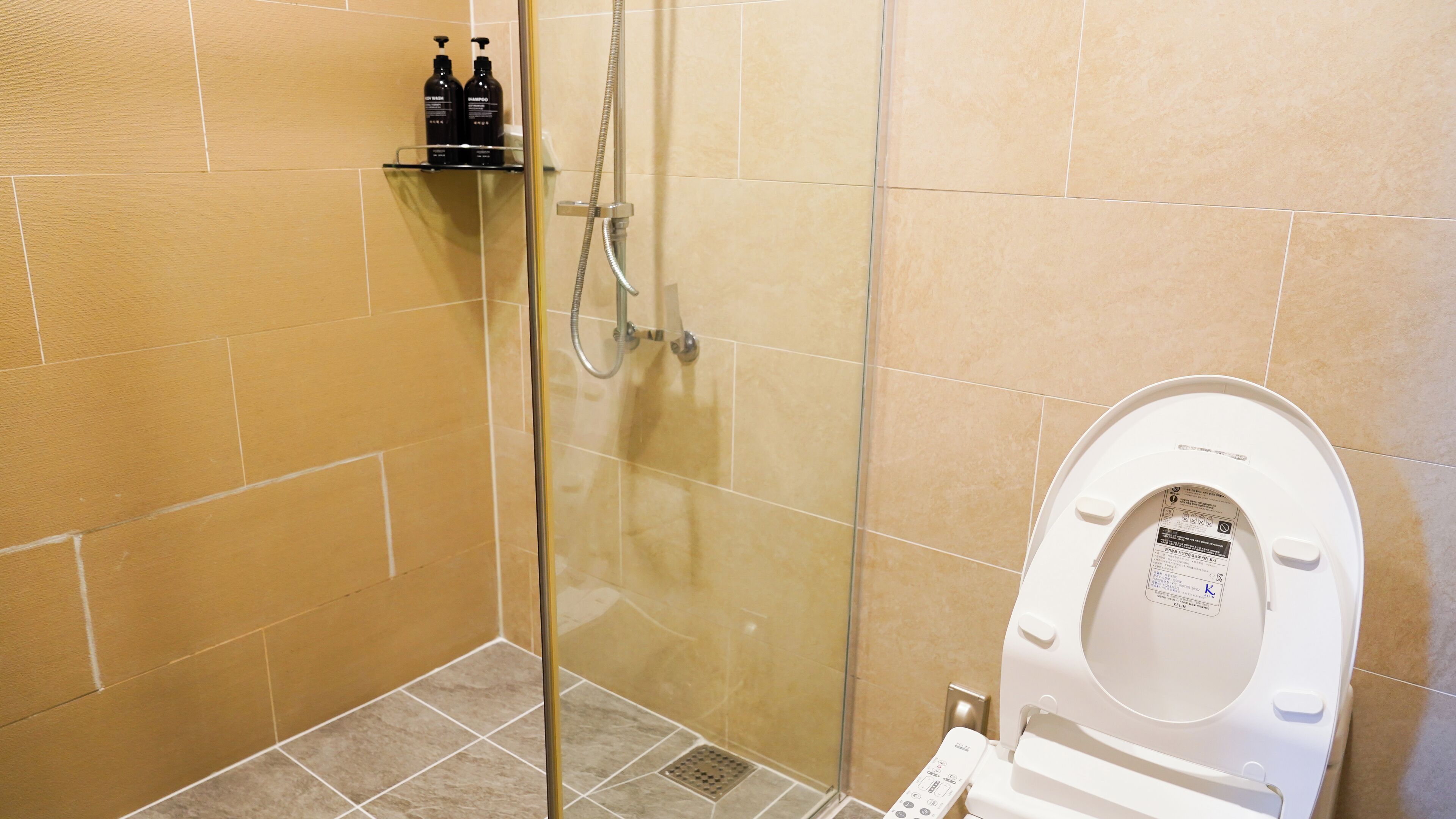 A bathroom with a glass-enclosed shower, a toilet, and a shelf with toiletries.