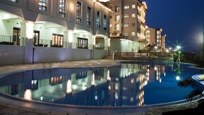 A swimming pool with a reflection of a multi-story building at night. - Sagewood Yeosu Gyeongdo Resort (Yeosu)