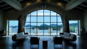 A spacious room with a large arched window offering a view of a lake and mountains. There are two sofas and a small table in the center. - Sagewood Yeosu Gyeongdo Resort (Yeosu)