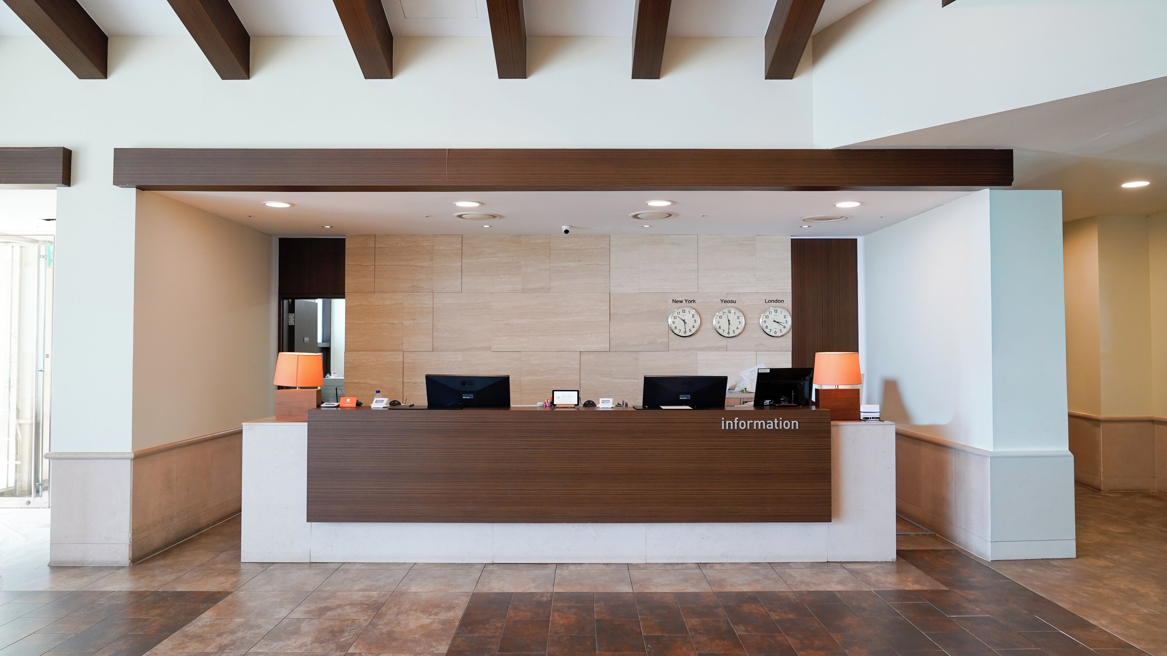 A reception desk with a wooden finish, two clocks displaying different time zones, and a sign labeled "information".