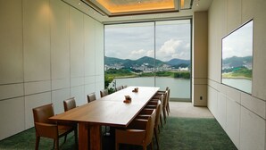 A conference room with a long table and chairs, large windows offering a view of a lake and distant cityscape. - Sagewood Yeosu Gyeongdo Resort (Yeosu)