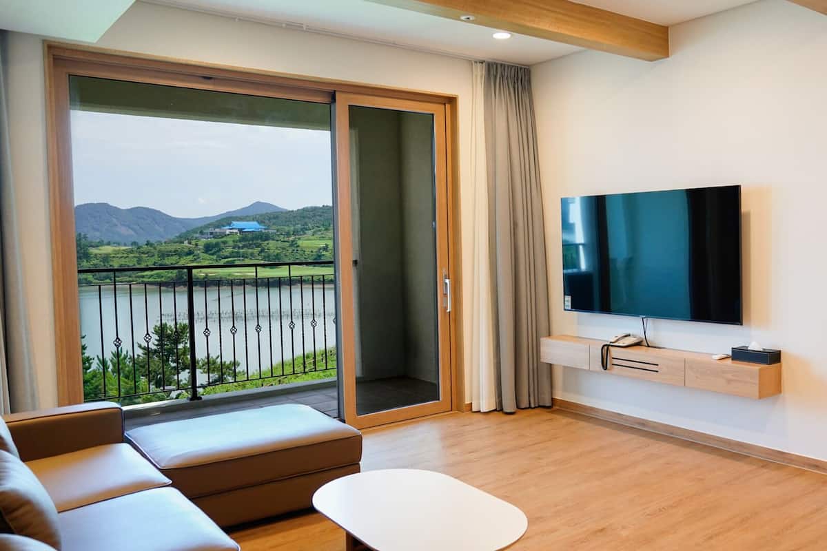 A modern hotel room with a large balcony, a flat-screen TV, a sofa, and a bed.