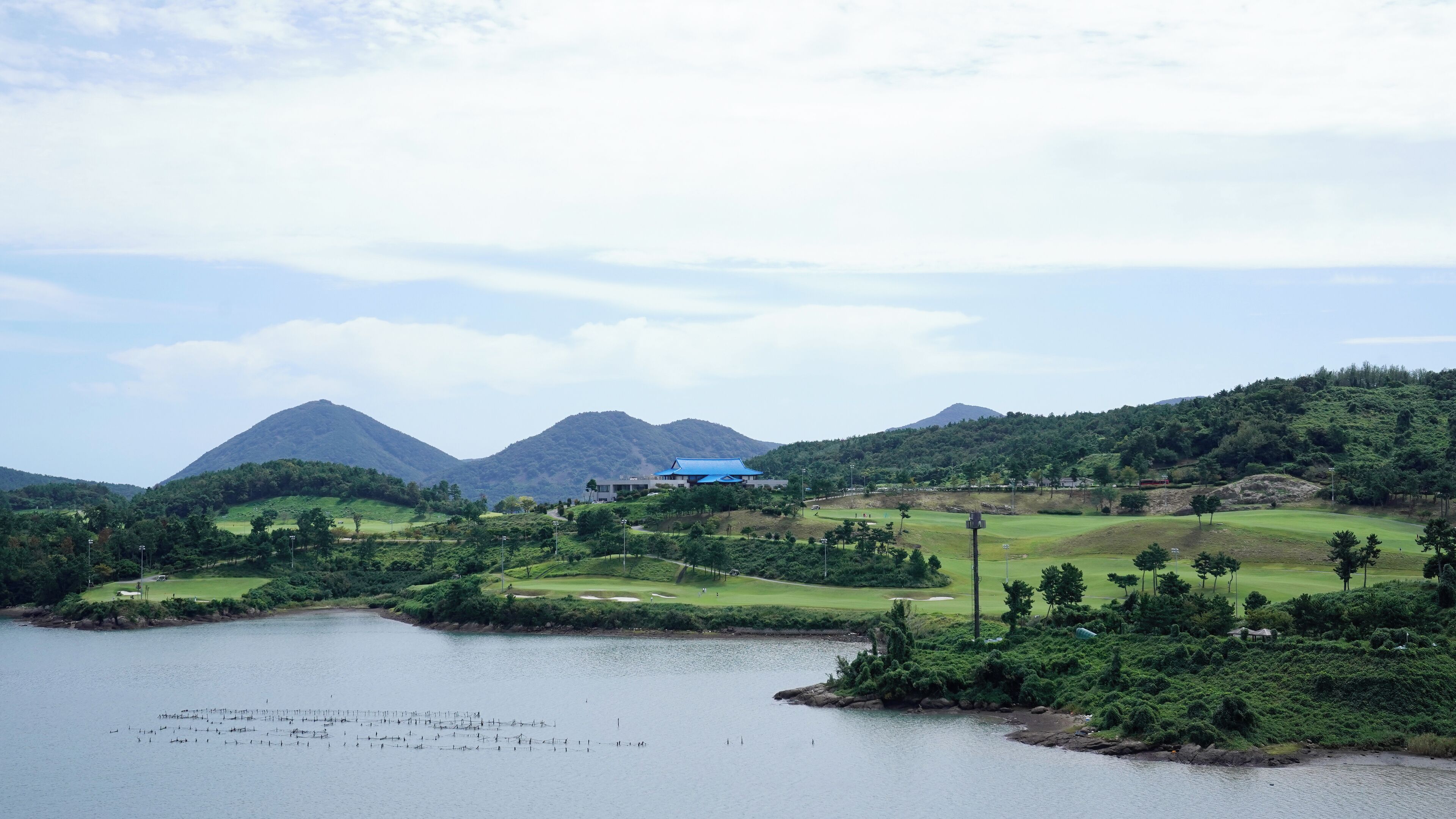 A golf course with a large building in the center, surrounded by lush greenery and mountains in the background.