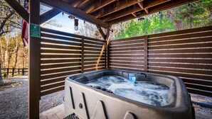 A hot tub under a wooden pergola with a view of trees and a sign indicating a shower before the hot tub. - Private 10-Hole Mini Golf, Bowling, Game Room, Arcade, Hot Tub, Playground (Sevierville)