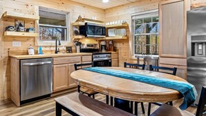 A wooden cabin kitchen with a wooden table, chairs, a dishwasher, a stove, a microwave, and a refrigerator. - Private 10-Hole Mini Golf, Bowling, Game Room, Arcade, Hot Tub, Playground (Sevierville)