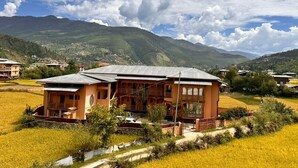 A two-story building with a flat roof, surrounded by fields and mountains in the background. - Paro Eco-Nest Resort (Paro)