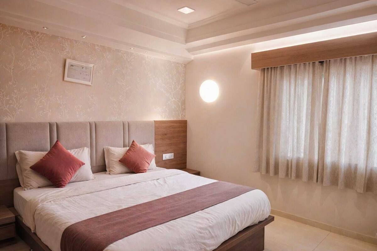 A bedroom with a bed, nightstands, a wall-mounted light, a window with curtains, and a framed certificate on the wall.