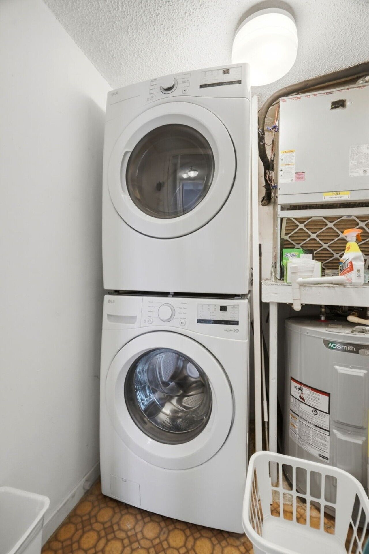 A laundry area with two stacked washing machines, a white chair, and a water heater.