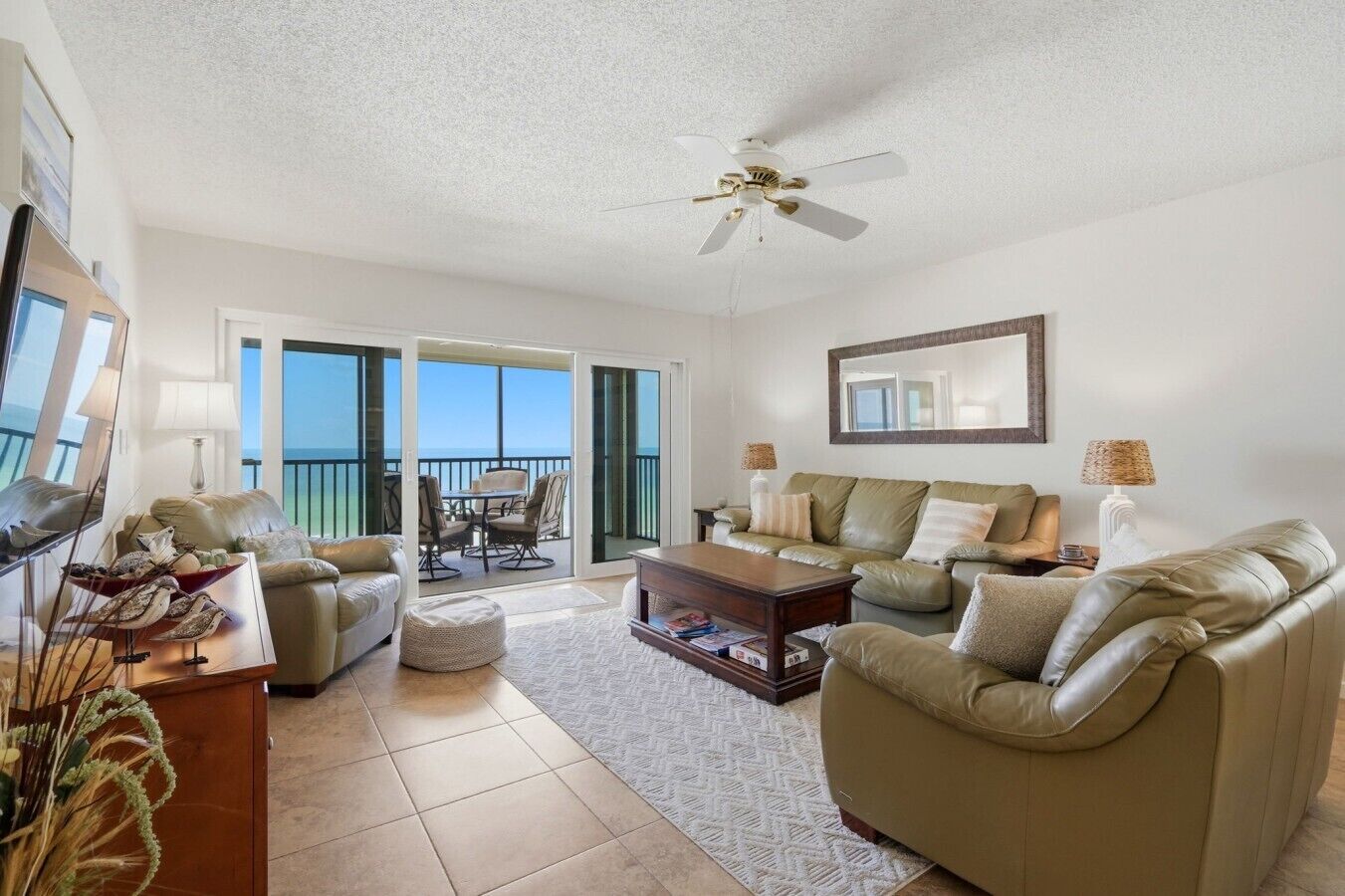 A spacious living room with a ceiling fan, a large window, and a balcony with a view.