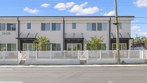 A two-story building with a white facade, numbered 2608, featuring a white picket fence, a small tree, and a visible power pole. - Upscale & Spacious Home 1 Mile to Ray-J | Casa Columbus (Tampa)