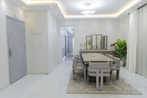 A modern dining area with a rectangular table and six chairs, a chandelier, and a potted plant. - 3-bedroom apartment in New Cairo (Cairo Governorate)