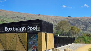 Un bâtiment portant l’inscription « Roxburgh Pool », avec un ciel dégagé et des collines en arrière-plan.