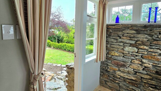 Habitación con pared de piedra, puerta que da al exterior y vista a un jardín.