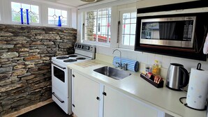 Una cocina con pared de piedra, armarios blancos, estufa, fregadero, microondas y una ventana con cortinas azules.