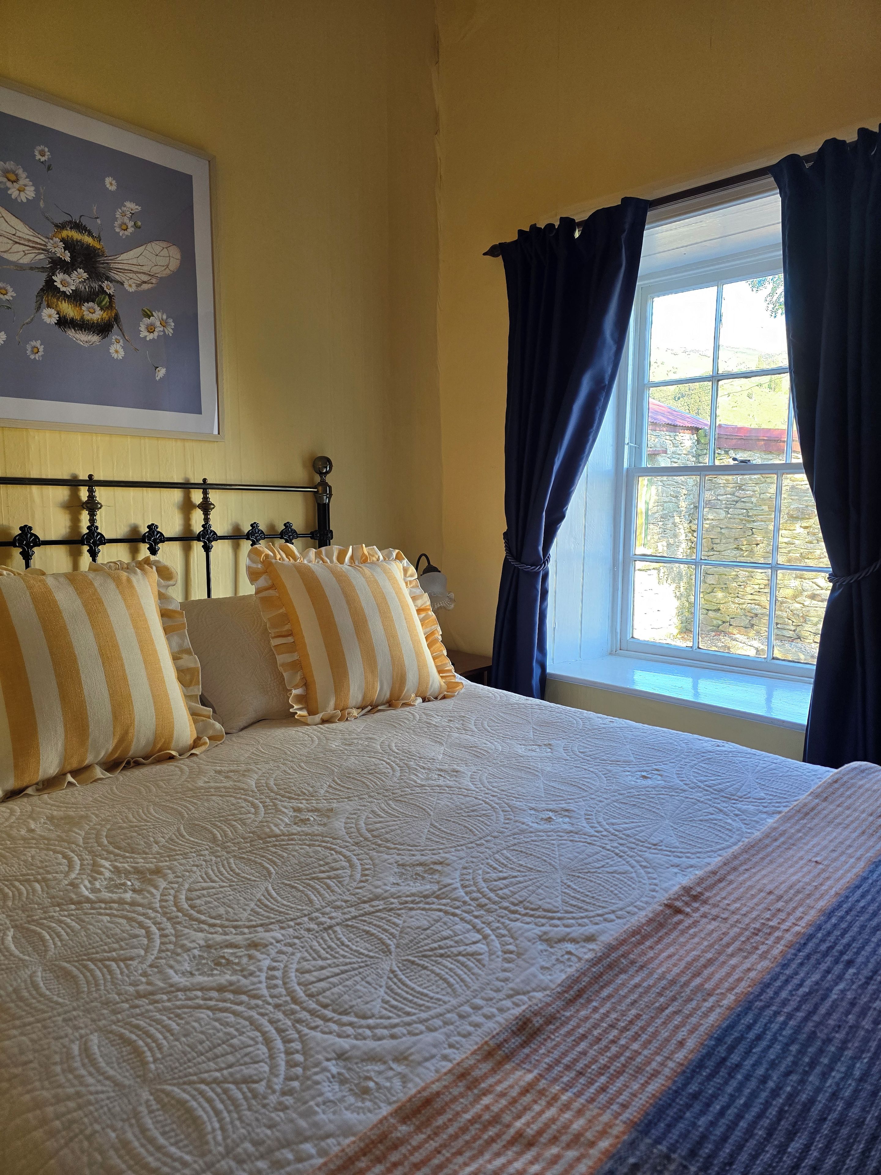 Un lit avec une couvre-lit à motifs, une tête de lit ornée d’un décor et une fenêtre avec des rideaux.