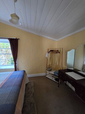 Une chambre à coucher avec un lit, une commode, un miroir et une fenêtre avec des rideaux.