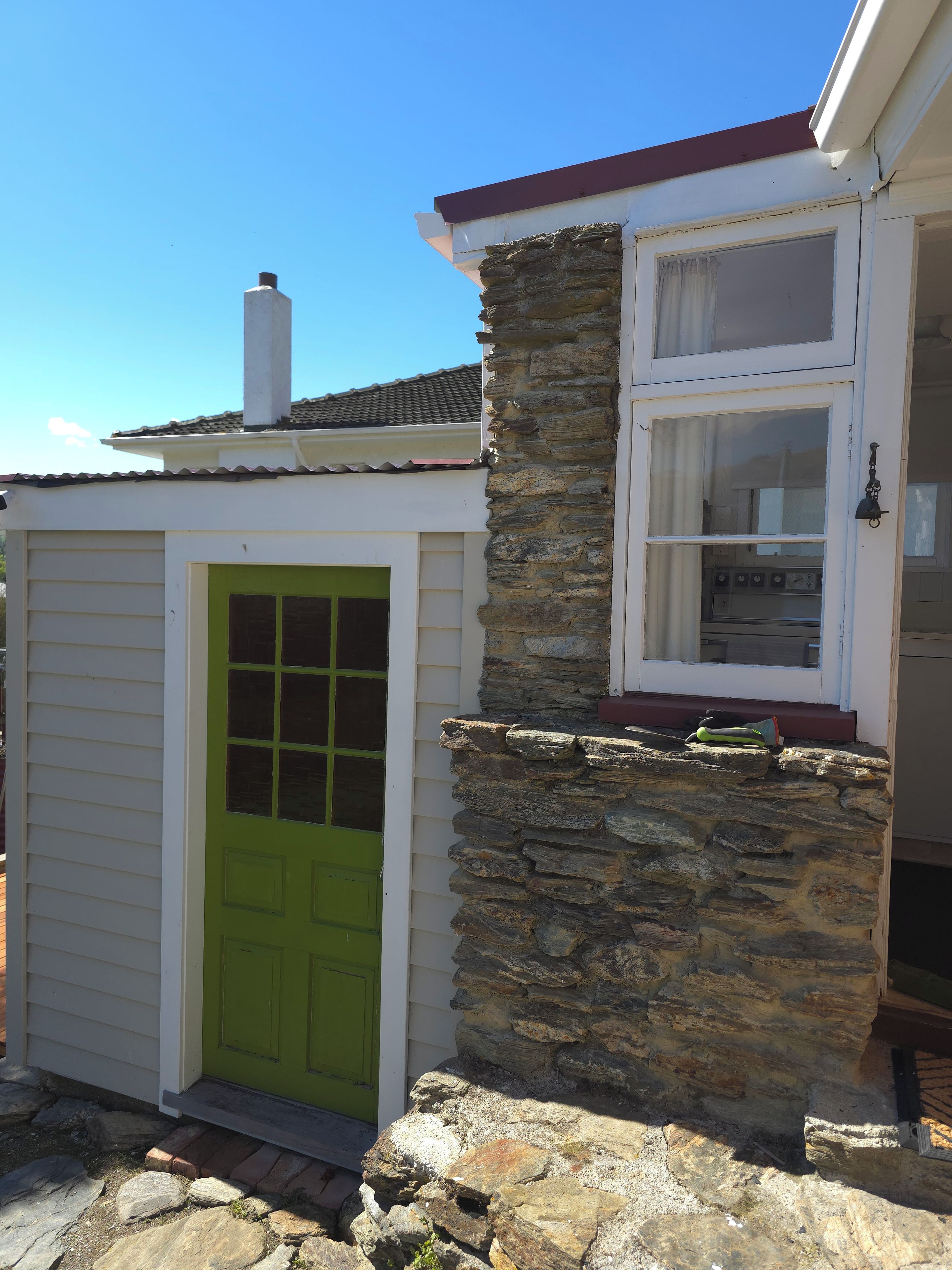 A house with a green door, a stone exterior, and a window with a white frame.