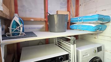 Uma área de lavanderia com uma secadora exaustor Haier branca, uma máquina de lavar frontal preta e um varal de metal.