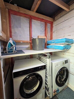 Un espace buanderie comprenant un sèche-linge à évacuation d’air blanc de la marque Haier, un lave-linge à chargement frontal noir et un étendoir métallique.