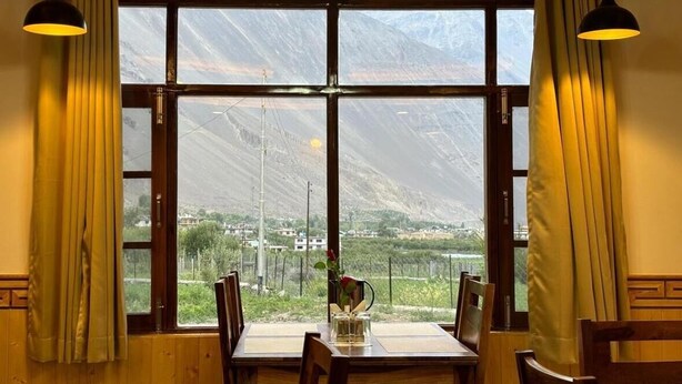 A dining area with a table and chairs, large windows with curtains, and a view of mountains.
