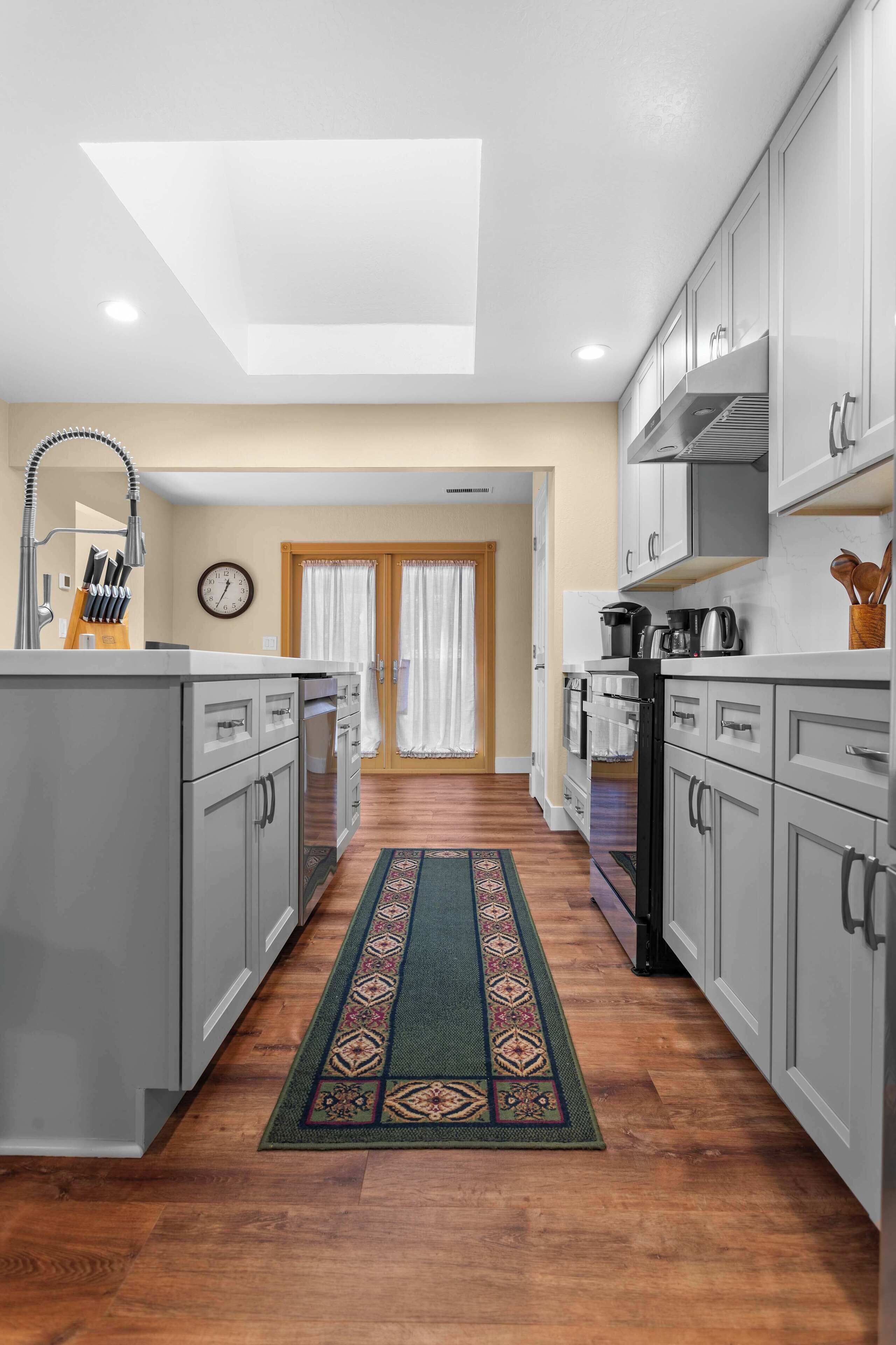 A modern kitchen with grey cabinets, a skylight, and a wooden floor.