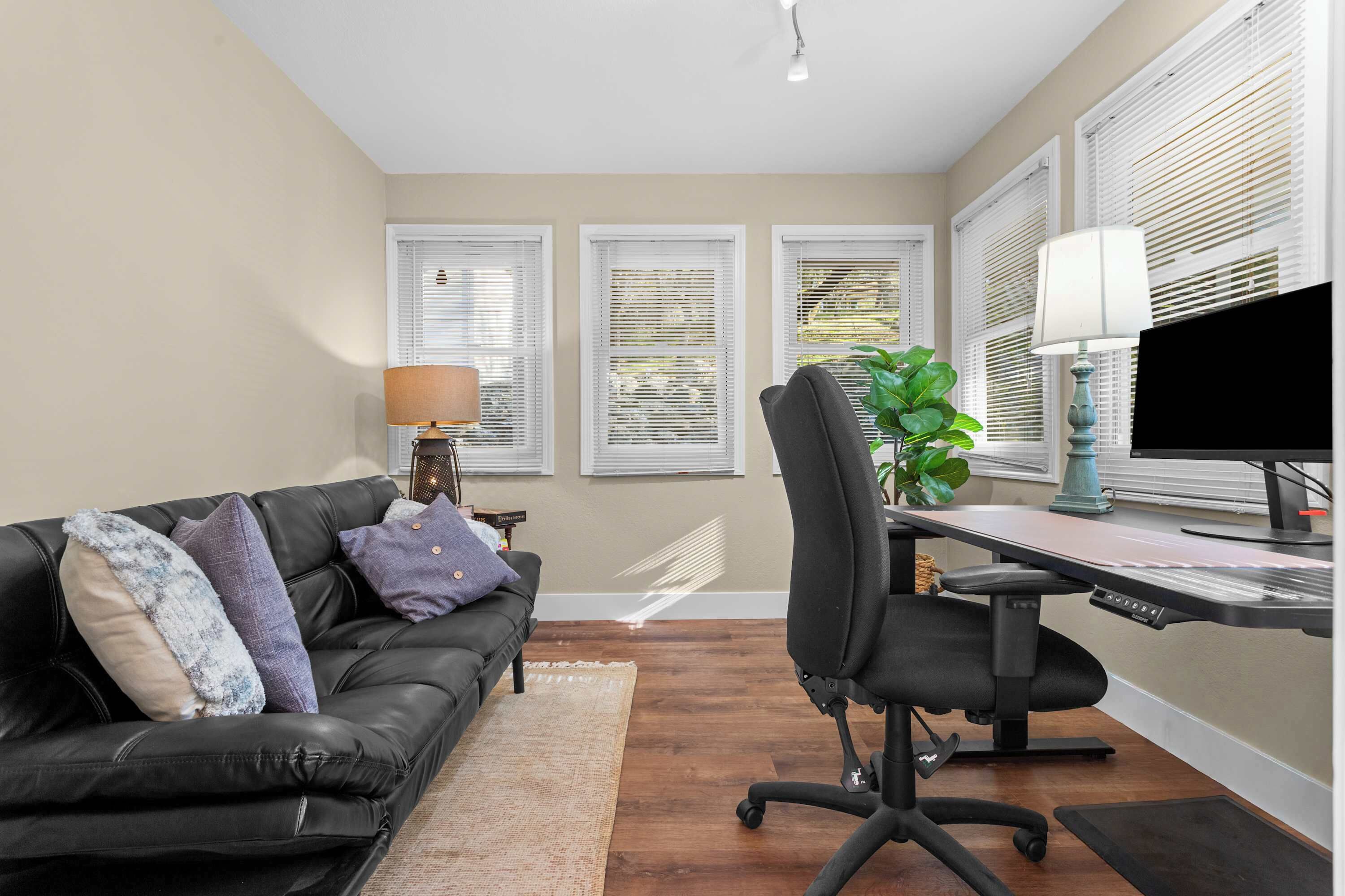 A modern office space with a black leather couch, a desk with a computer, and a plant.