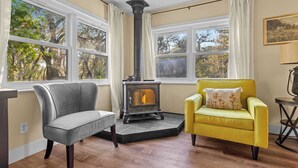 Une pièce avec une cheminée, deux fauteuils, de grandes fenêtres et un ventilateur de plafond.