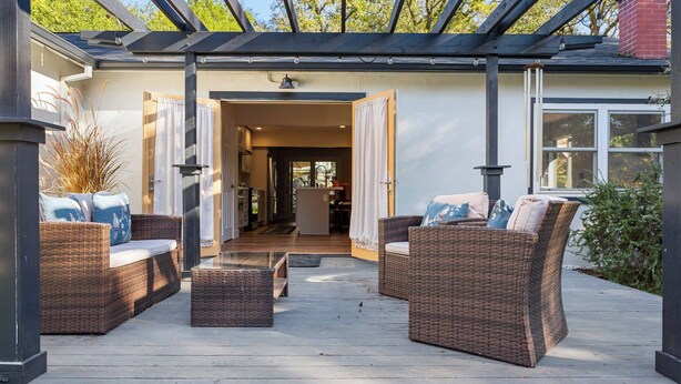 Une terrasse extérieure couverte, aménagée avec des meubles en osier et dotée d’un toit en verre.