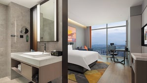 A modern hotel room with a large bed, a double sink, a large mirror, a desk, and a view of the city. - Hampton by Hilton Hangzhou Liangzhu (Hangzhou)