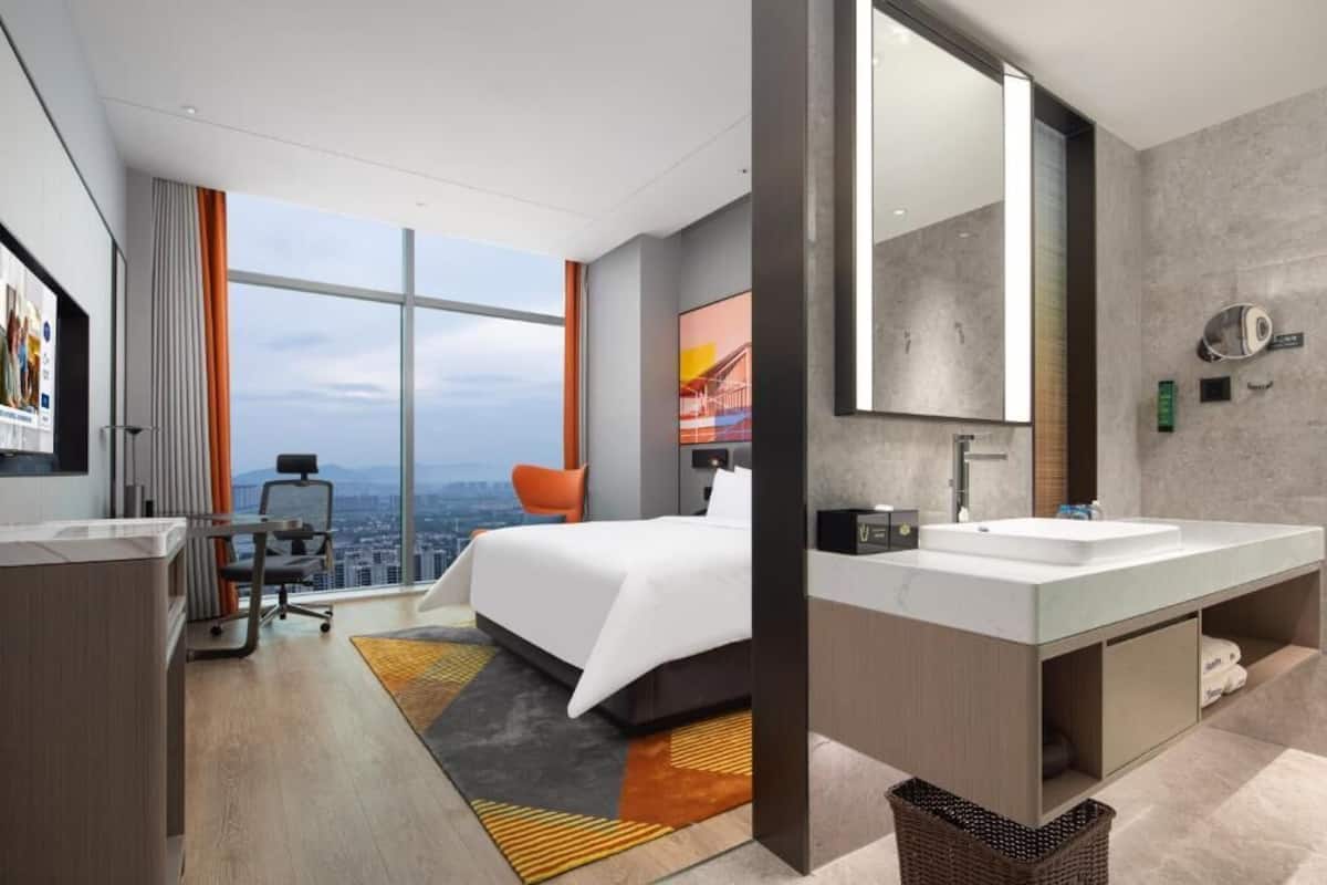 Ein modernes Hotelzimmer mit einem großen Bett, zwei Waschbecken, einem großen Spiegel und Blick auf die Stadt.