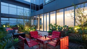An outdoor seating area with red chairs and tables, surrounded by plants and a modern building with large windows. - Hampton by Hilton Hangzhou Liangzhu (Hangzhou)
