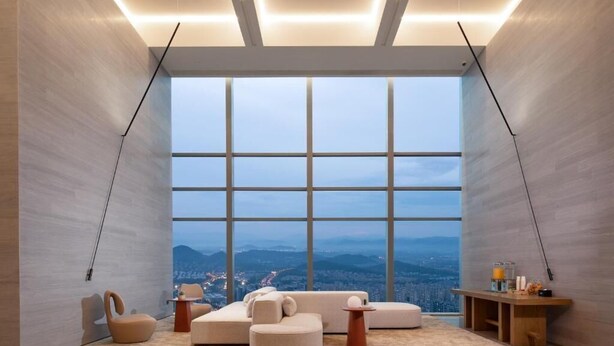 A modern interior with a large panoramic window, a sectional sofa, a small table, and a unique chair. - Hampton by Hilton Hangzhou Liangzhu (Hangzhou)