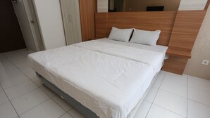 Un letto rifatto con cura in una camera d'albergo, con testiera in legno, biancheria da letto bianca e pavimento piastrellato.
