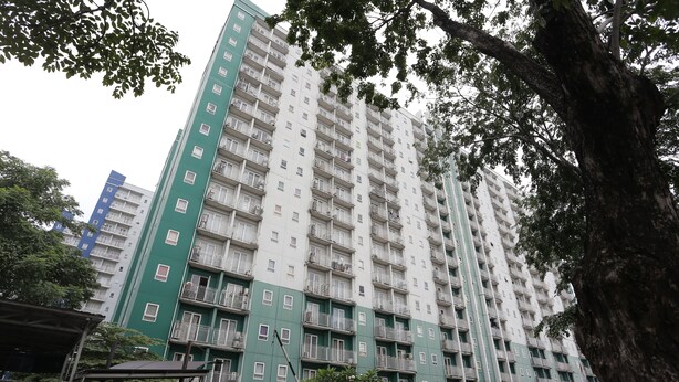 Un edificio residenziale a più piani con balconi, una facciata verde e un'area circostante alberata con auto parcheggiate.