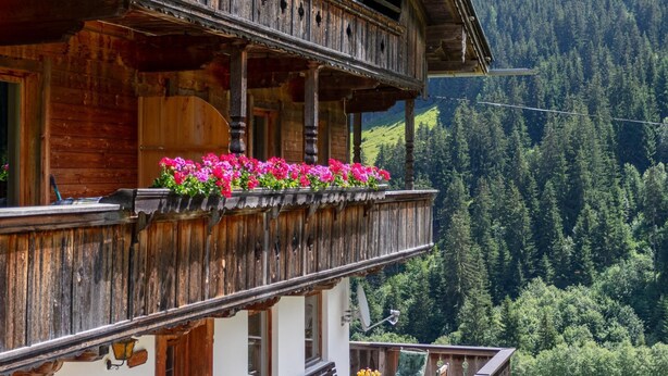 A wooden chalet with a balcony, surrounded by a forested mountain landscape. - Two holiday apartments in farmhouse with a view (Alpbach)