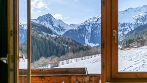A mountain view from a cabin with a wooden interior and a window overlooking snow-covered slopes and a small building. - Two holiday apartments in farmhouse with a view (Alpbach)