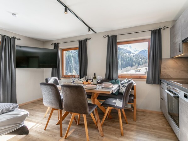 Un comedor moderno con una mesa dispuesta para cuatro, un televisor en la pared y vistas a un paisaje montañoso a través de amplios ventanales.