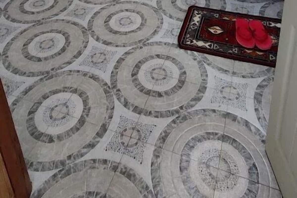 Une petite pièce, peu meublée, avec un sol à motifs, un lit, une chaise et un sac suspendu.