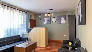 A modern living room with a sofa, a coffee table, and a reception desk. There are wall-mounted lights and artwork. - Miriam Inn Chaka (Chaka)
