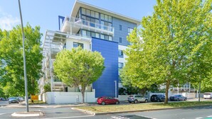 Un edificio moderno con fachada azul, una acera y un estacionamiento con automóviles.
