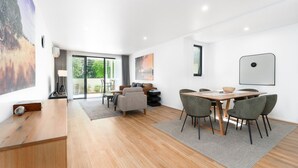 Una habitación moderna y bien iluminada con una mesa de comedor de madera, sillas grises, un sofá y un amplio ventanal con vistas a la vegetación.
