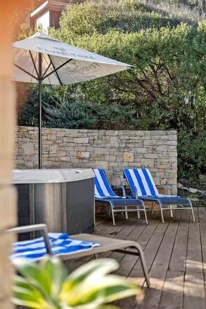 A patio with two lounge chairs and a table, a stone wall, and a large umbrella. - Sandbanks | Beachfront w/Spa & Ocean Views (Separation Creek)