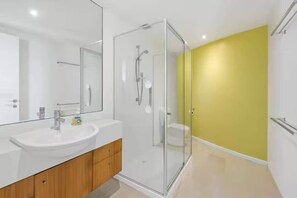 A modern bathroom with a glass shower enclosure, a white sink, and a yellow accent wall. - Sandbanks | Beachfront w/Spa & Ocean Views (Separation Creek)