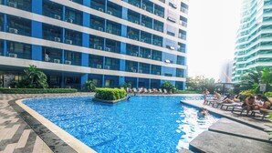 A swimming pool with a tiled deck, surrounded by a modern building with balconies and air conditioning units. - Air residence Makati Air Luxury Package (Makati)