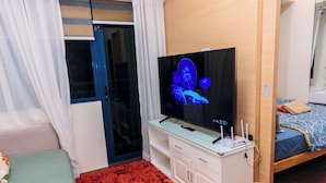 A compact hotel room with a bed, a TV, a small desk, and a sliding door leading to a balcony. - Air residence Makati Air Luxury Package (Makati)