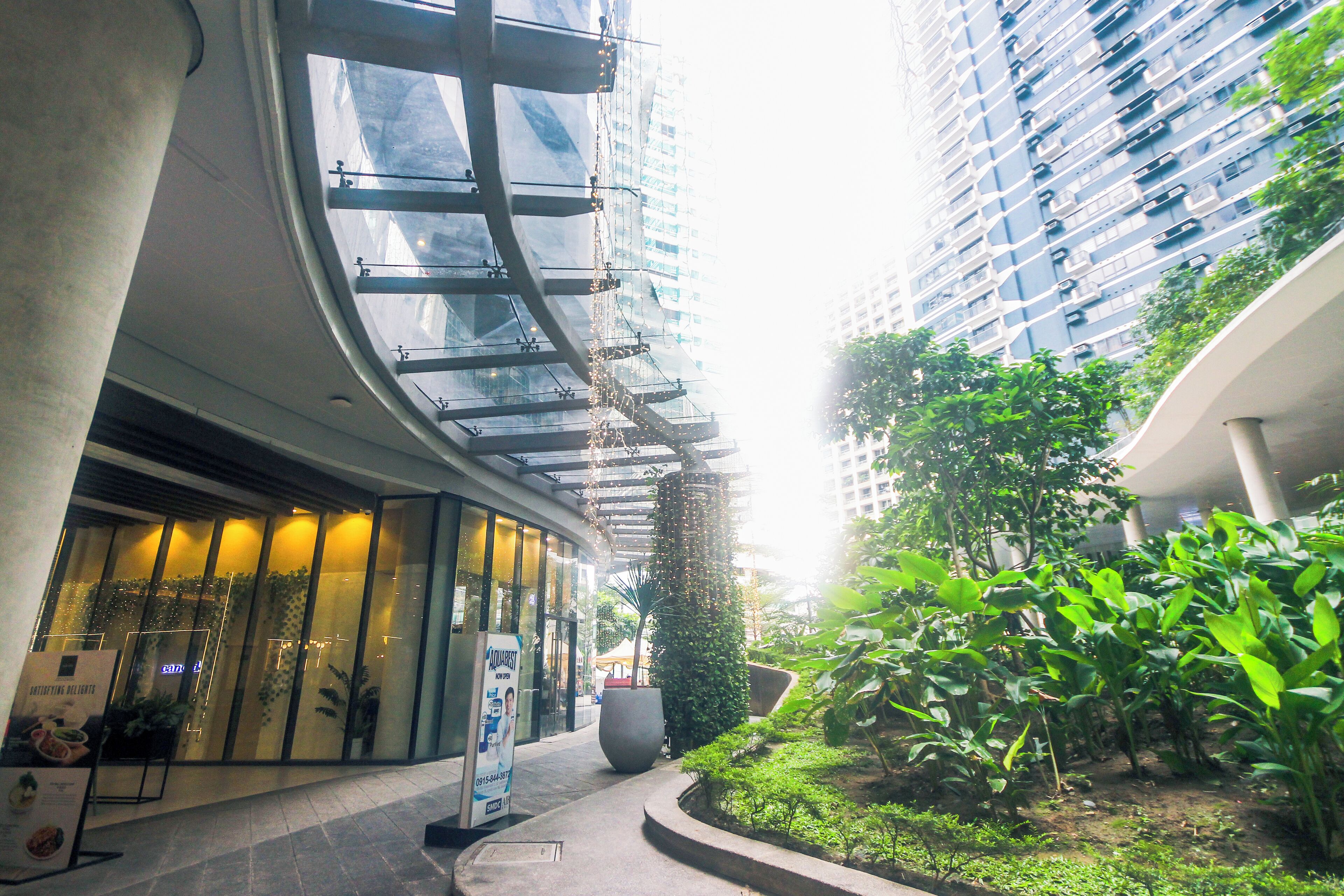 Un edificio moderno con fachada de vidrio, entrada curva y un jardín bien cuidado.